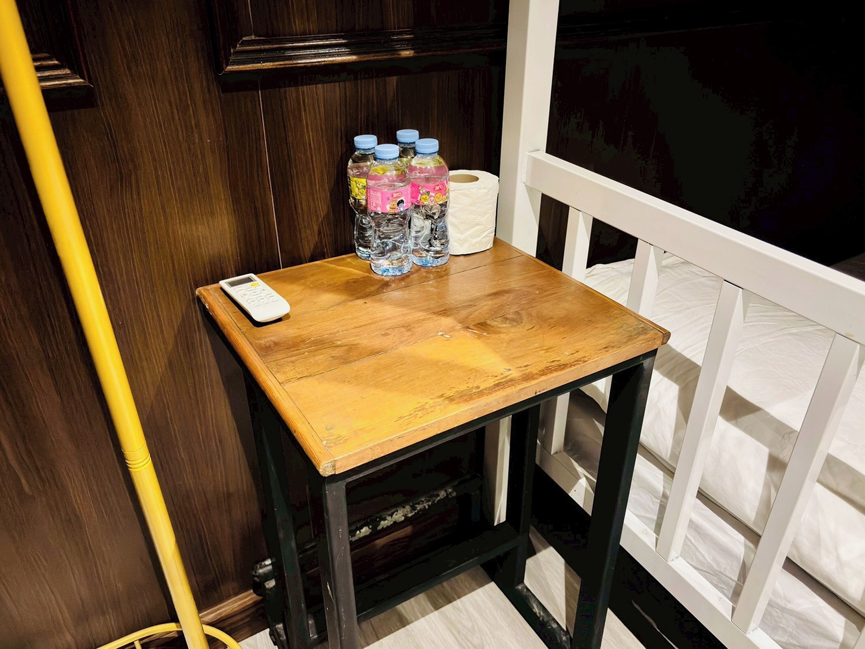 A wooden table with a white scale, bottles of water, and a roll of toilet paper.