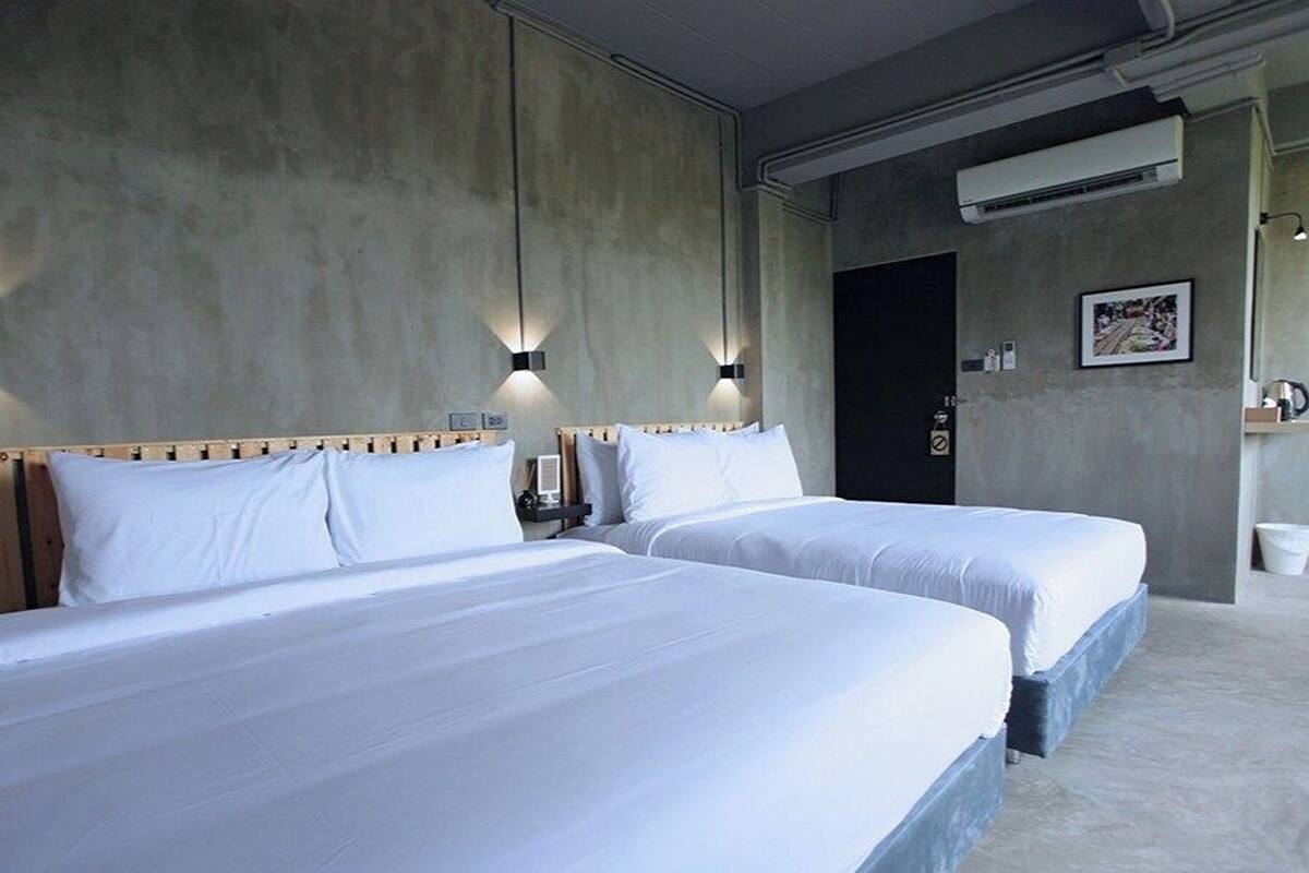 A hotel room with two beds, a concrete wall, and a door.