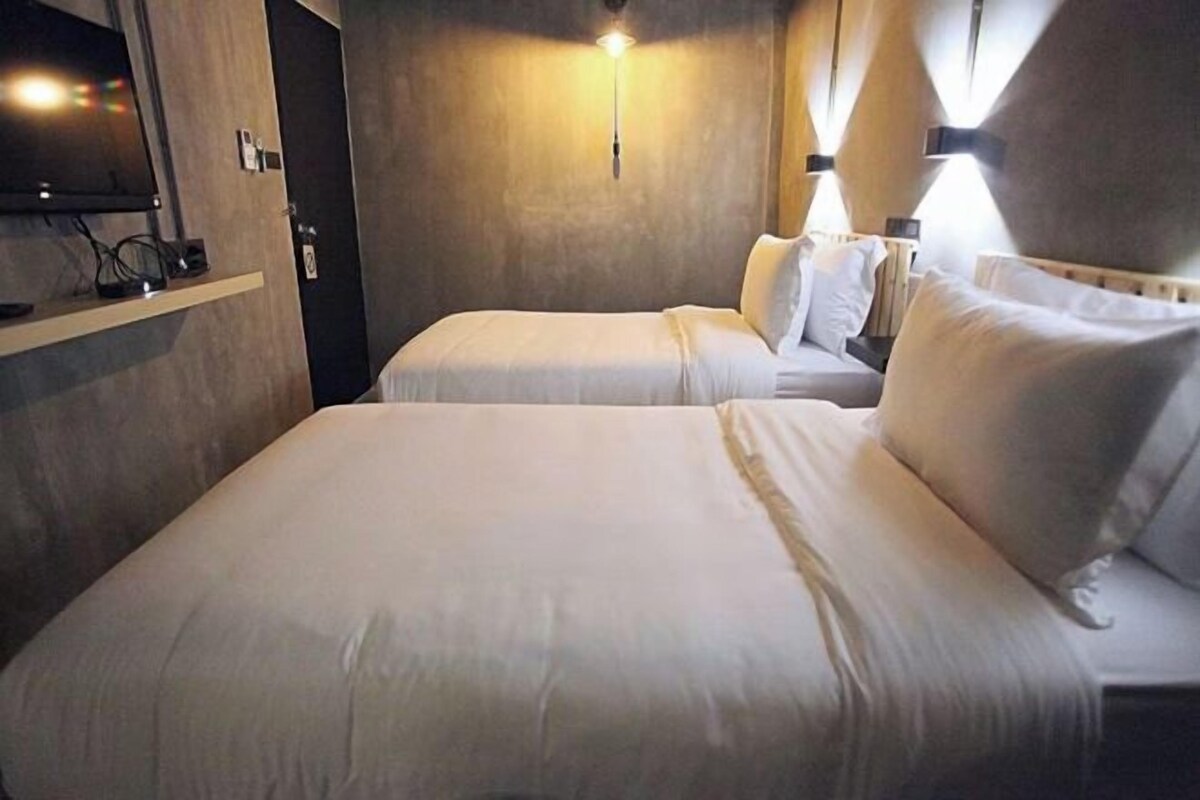 A hotel room with two beds, a TV on a shelf, and wall-mounted lighting.