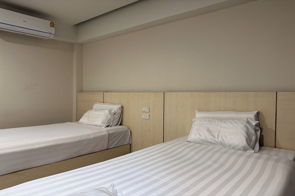 A hotel room with two single beds, a wooden headboard, and an air conditioning unit on the wall.