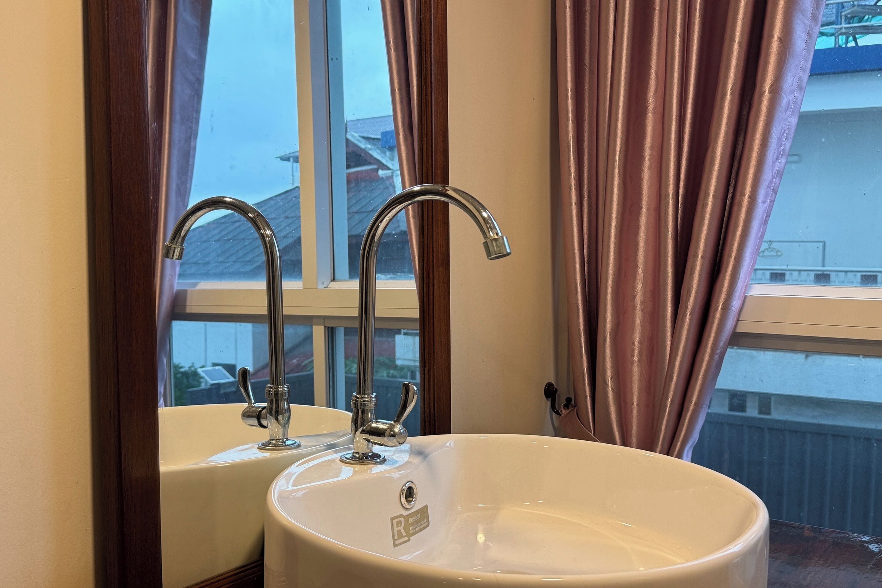 A bathroom with a double sink, a window, and curtains.
