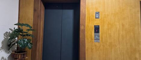 An elevator with a wooden finish, a potted plant beside it, and a wall-mounted intercom system.