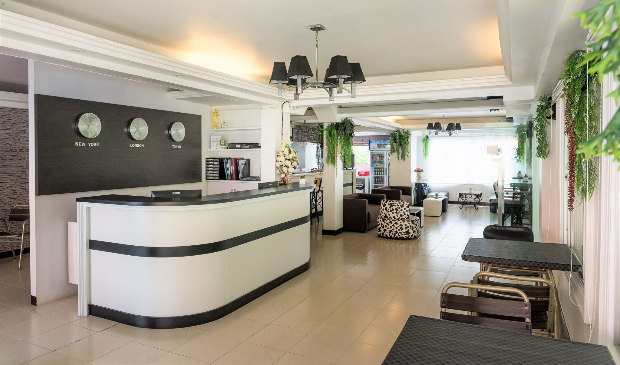 Een moderne hotellobby met een receptiebalie, een kroonluchter en een zithoek met tafels en stoelen.