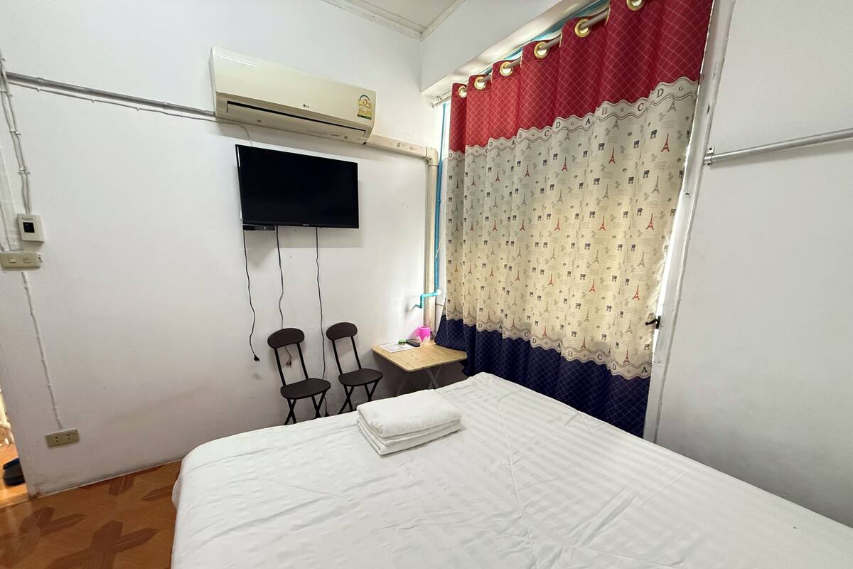 A hotel room with a bed, a desk, two chairs, a television, and an air conditioning unit.