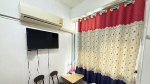 Une chambre comprenant un lit, un bureau, deux chaises, une télévision et un climatiseur.