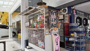 Un café proposant un tableau des prix, une machine à café, ainsi qu’une variété de boissons et d’en-cas.