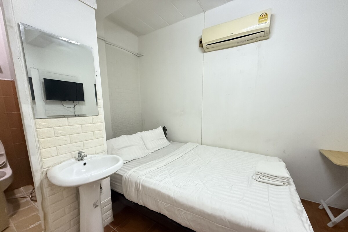 Una habitación pequeña y limpia con una cama individual, un lavamanos blanco y un aire acondicionado instalado.