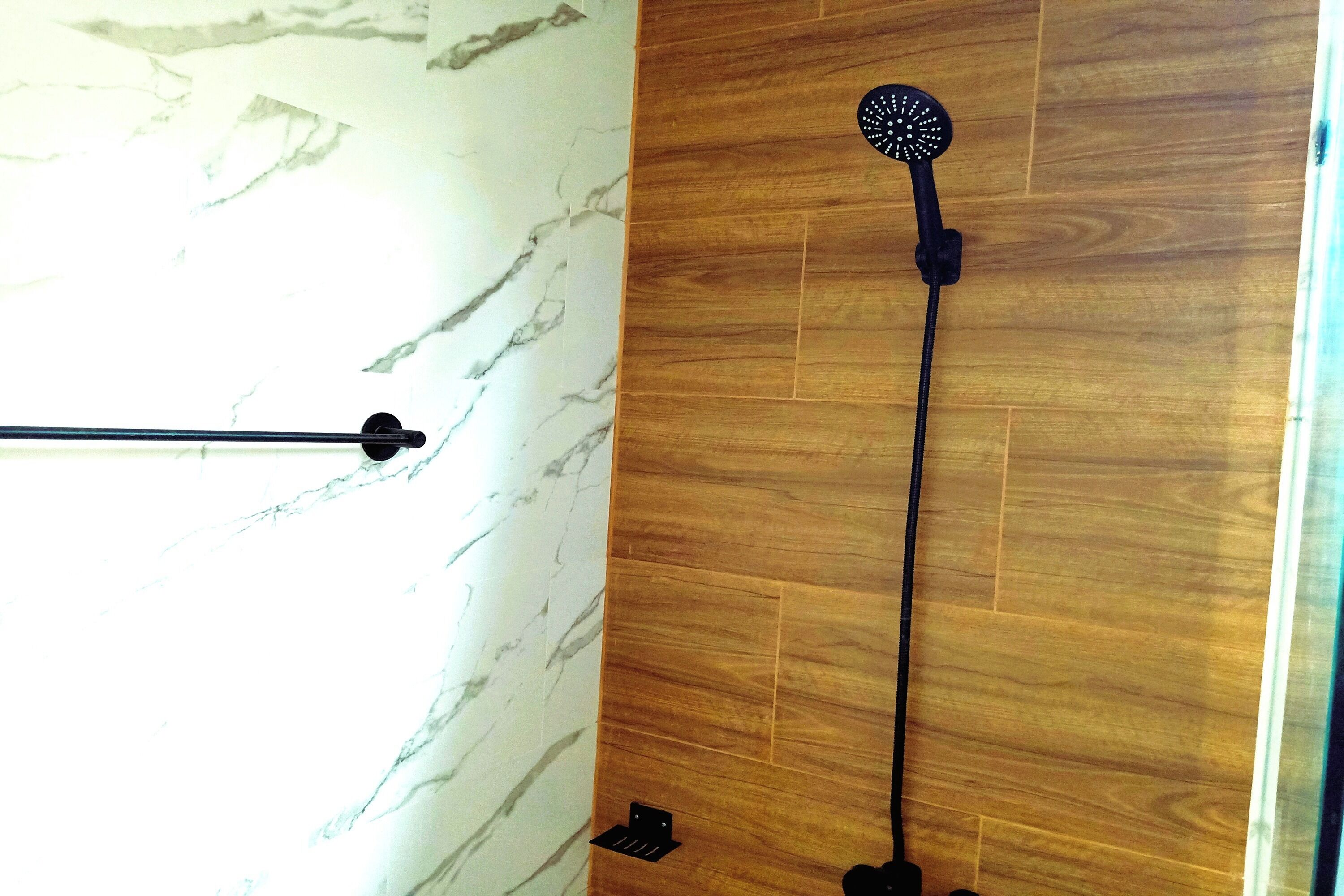 A bathroom with a wooden floor, a marble wall, and a shower with a black handheld showerhead.
