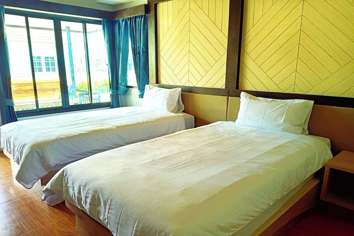 Une chambre d’hôtel avec deux lits, un plancher en bois et une grande fenêtre avec des rideaux.