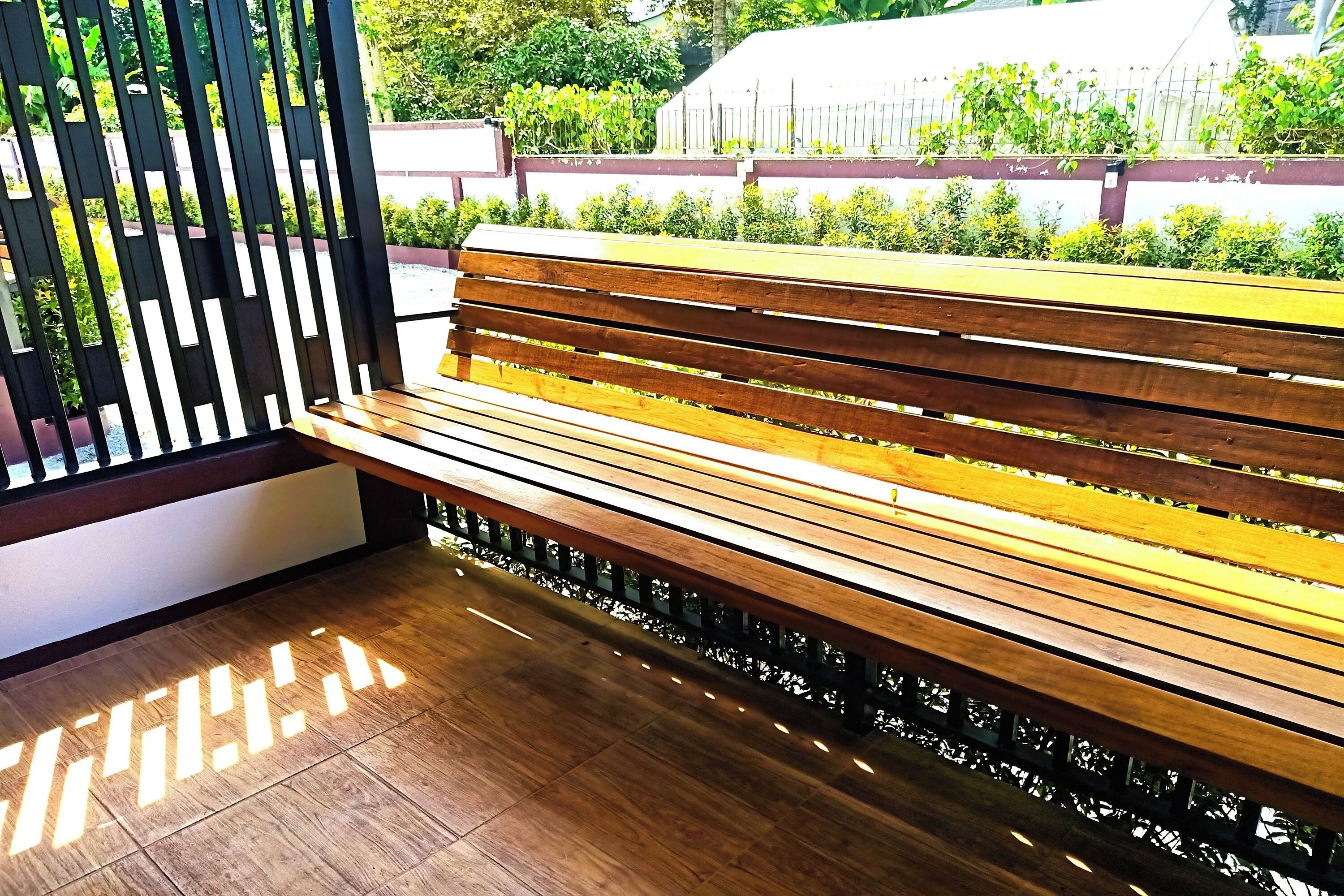 A wooden bench with a metal frame, positioned next to a white wall with a black decorative panel.