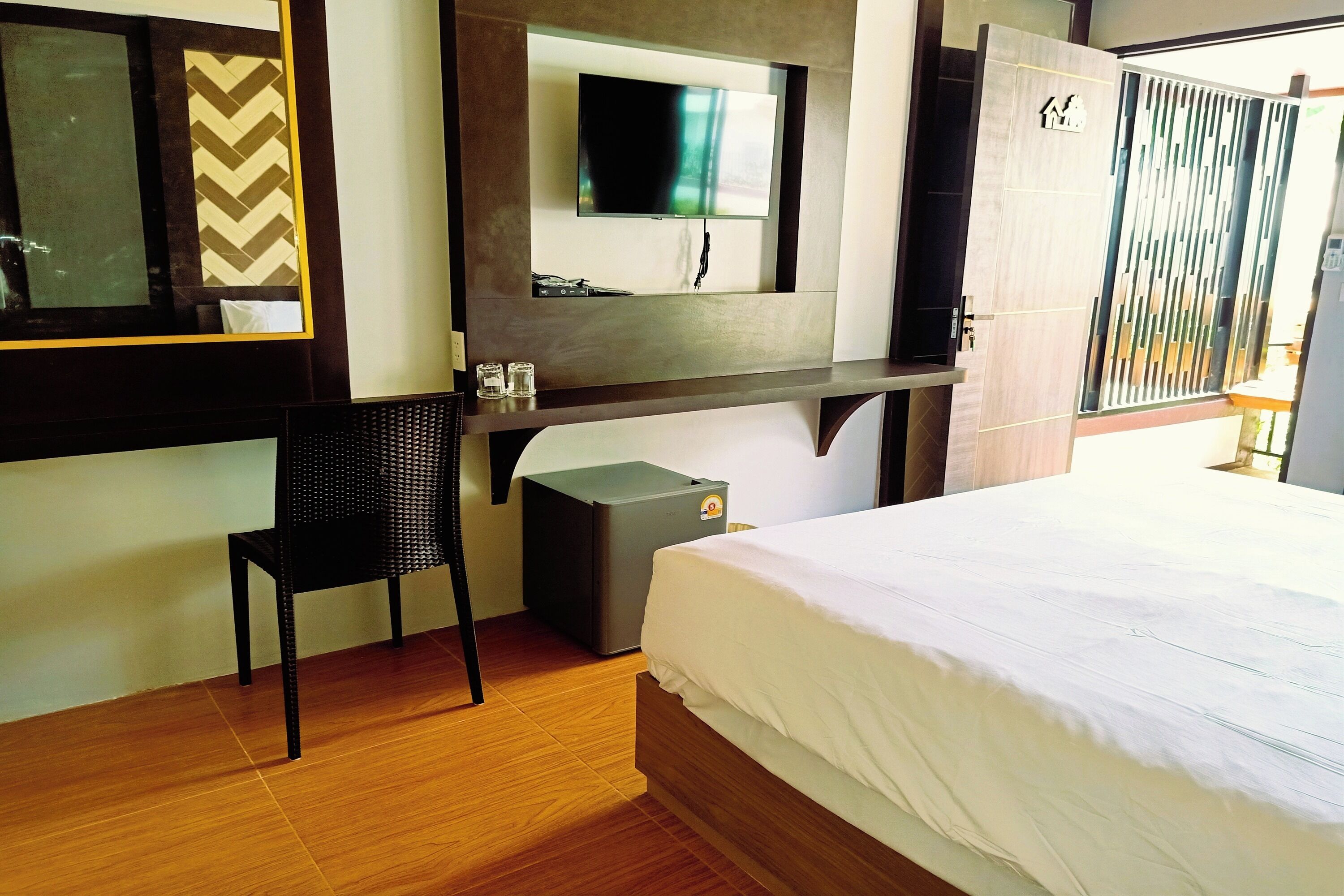 Habitación de hotel con cama, escritorio, silla, televisor montado en la pared y armario.