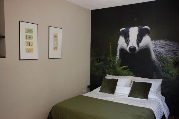 Ein Schlafzimmer mit einem Bett, zwei gerahmten Bildern an der Wand und einem großen Wandgemälde von einem Dachs.