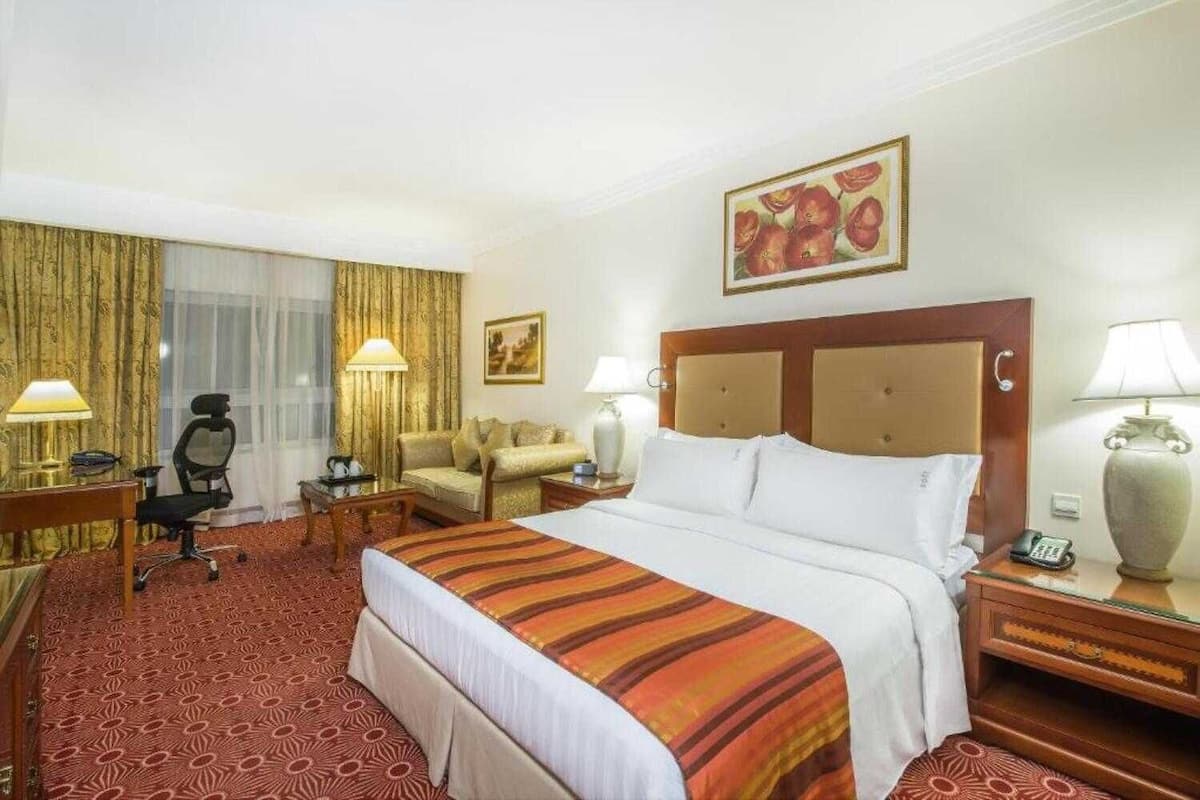 A hotel room with a large bed, a desk with a chair, a sofa, and a painting on the wall.