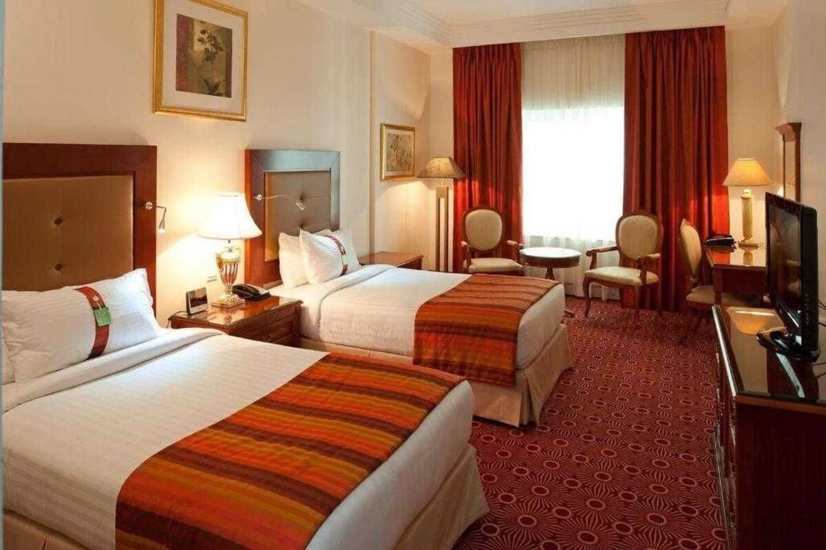 A hotel room with two beds, a desk, a chair, a TV, and a window with curtains.