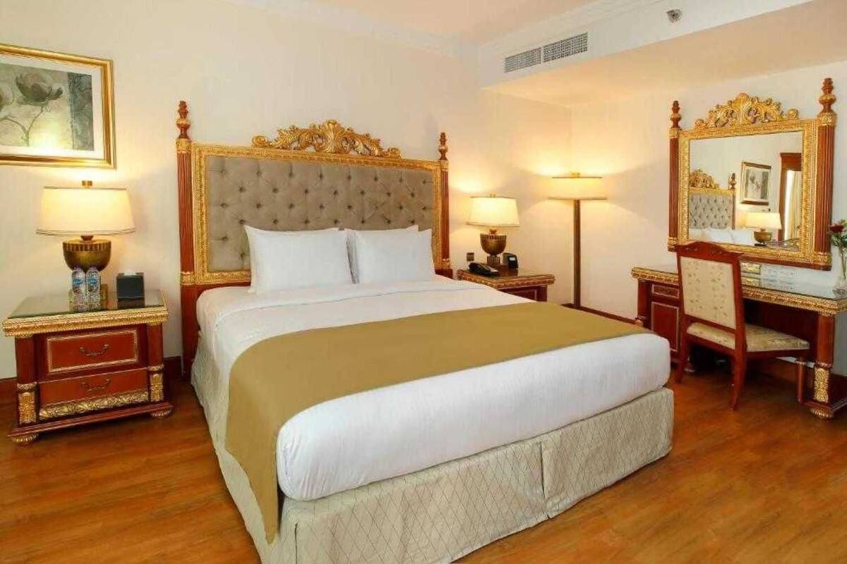 A hotel room with a large bed, two bedside tables, a dresser, and a large mirror.
