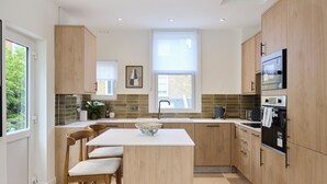 Una cocina moderna con armarios de madera, una isla central con taburetes, horno empotrado y ventana que proporciona luz natural.