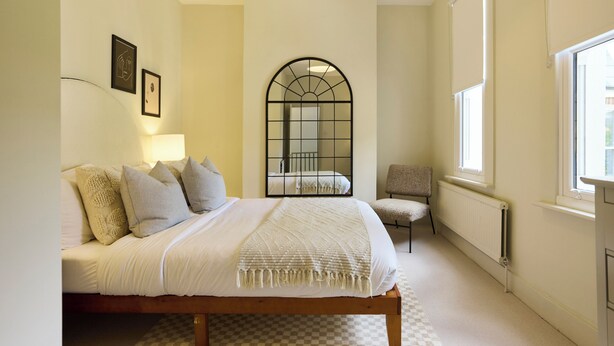 Un dormitorio con cama, una silla, un radiador y una ventana.