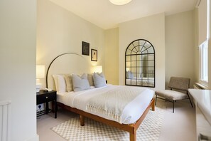 Quarto com cama, mesa de cabeceira, luminária, cadeira e uma janela grande com vista.