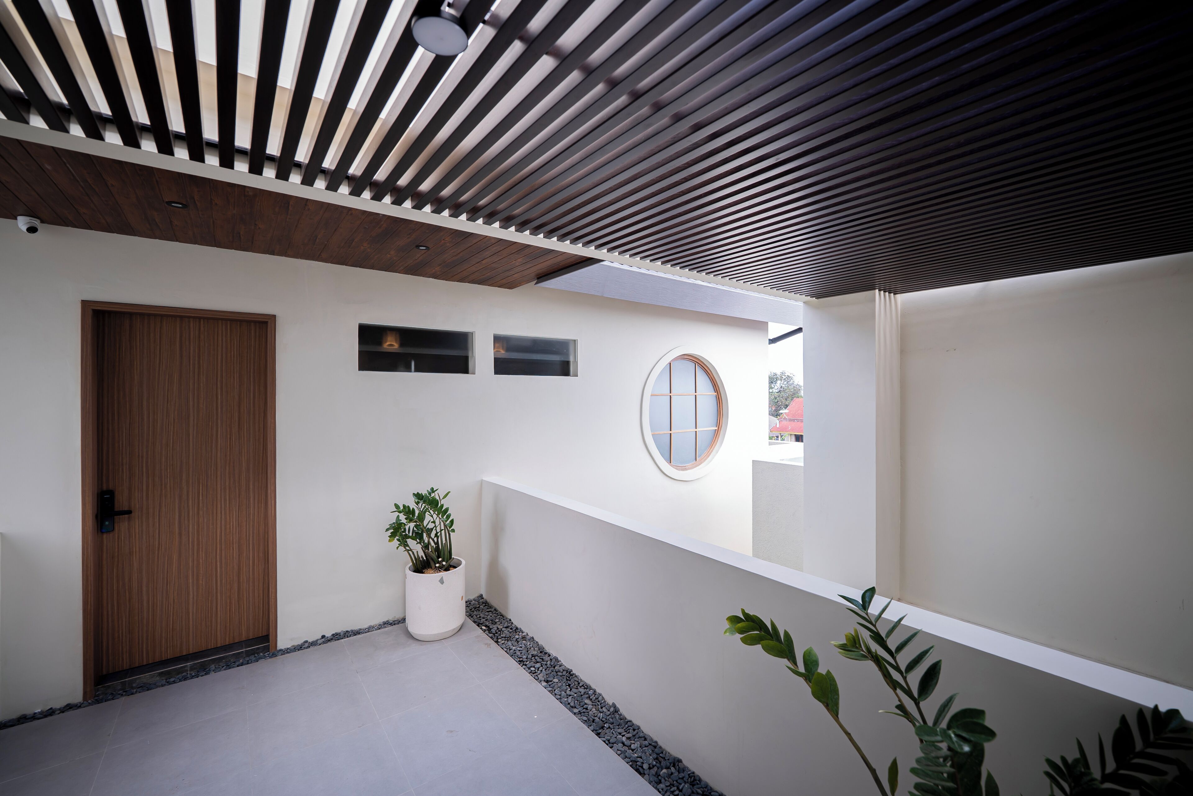 A modern exterior with a wooden door, a potted plant, and a circular window.