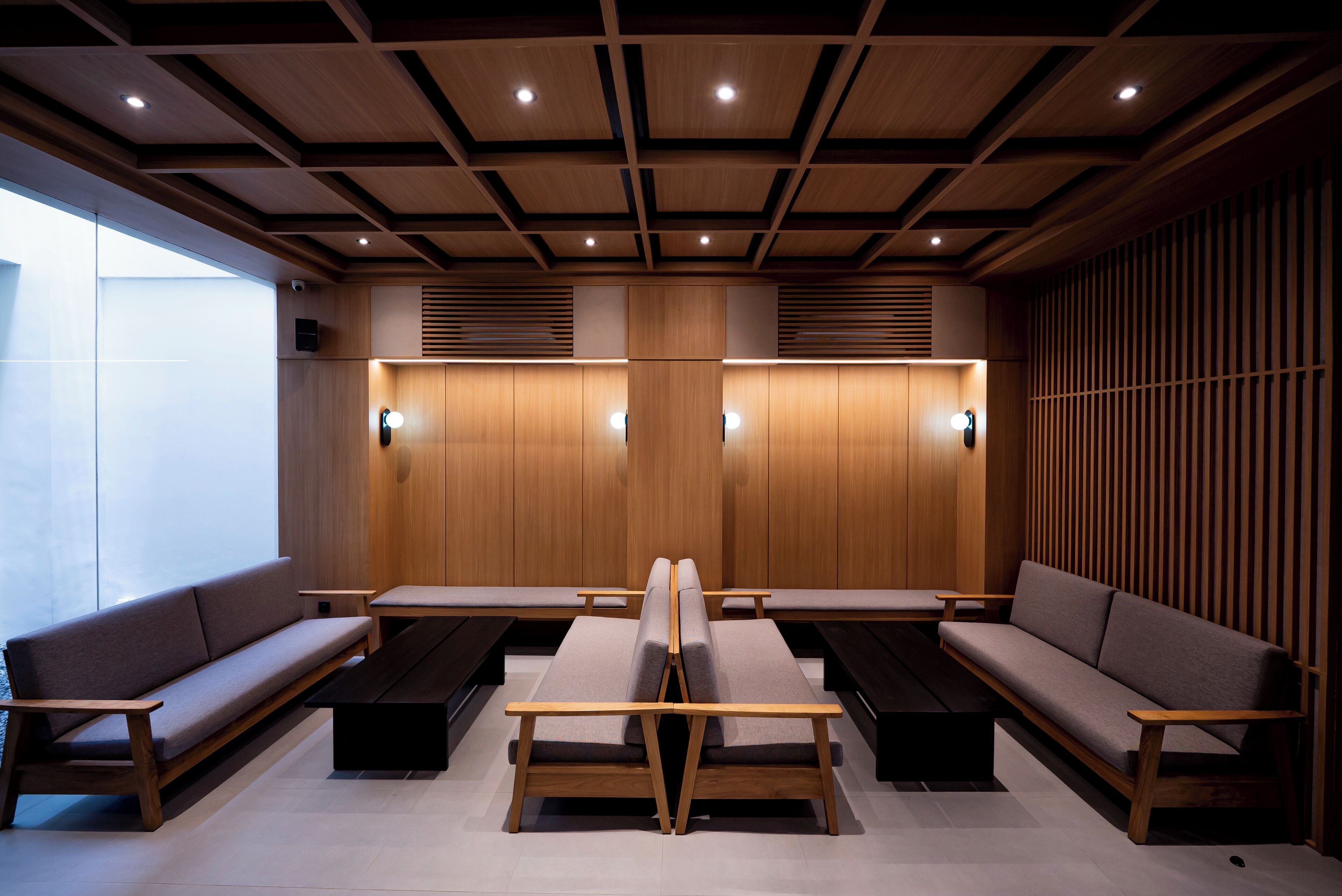 A modern waiting area with wooden paneling, cushioned seating, and built-in lighting.
