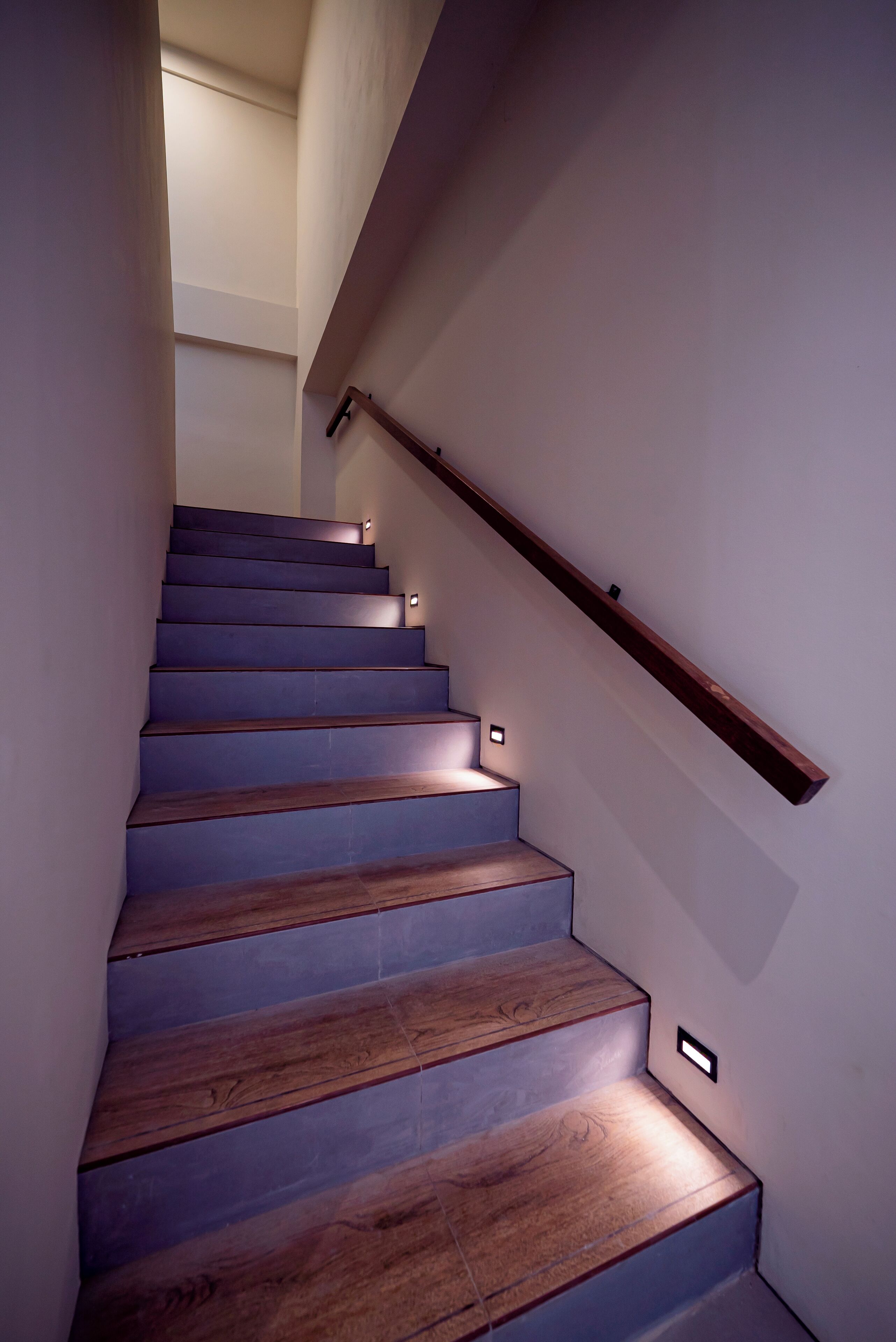 A staircase with wooden steps and a wooden handrail, illuminated by small lights along the handrail and steps.