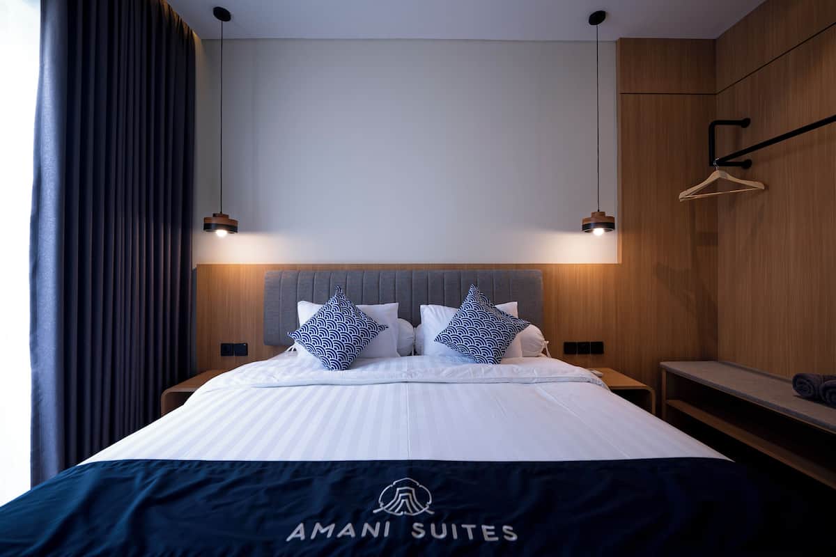 Una habitación de hotel moderna con una cama bien hecha, dos lámparas colgantes y un cabecero de madera.