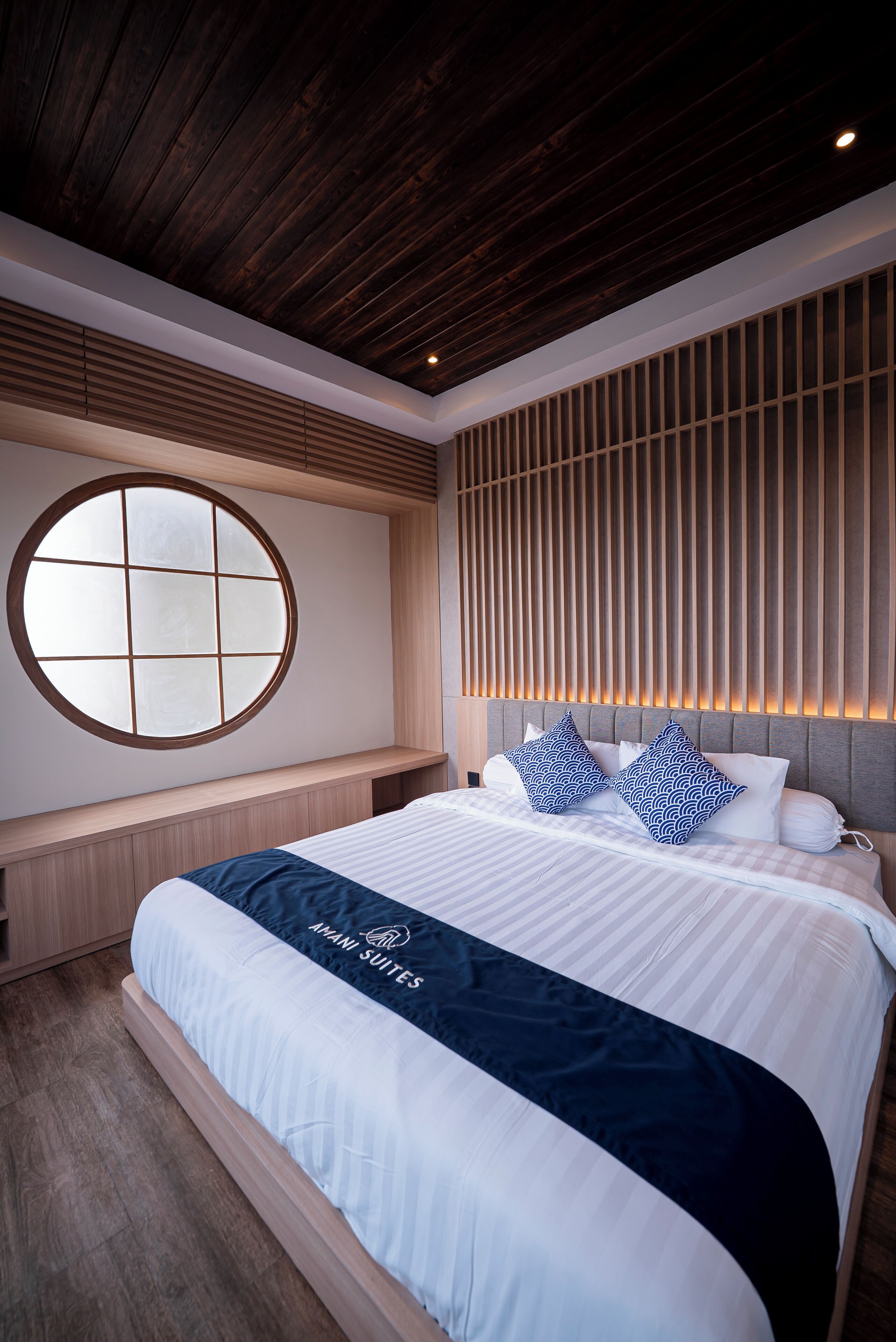 Ett modernt hotellrum med en stor säng, ett runt fönster, träpanel och ett sängöverkast med ett välkänt varumärke.