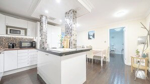 A modern kitchen with white cabinets, a black microwave, and a tiled backsplash. - Vale royale (London)