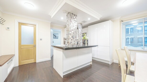 A modern kitchen with a central island, white cabinetry, and a large window providing natural light. - Vale royale (London)