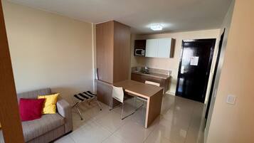 A compact living space with a kitchenette, a sofa with cushions, a dining table, and a small chair.