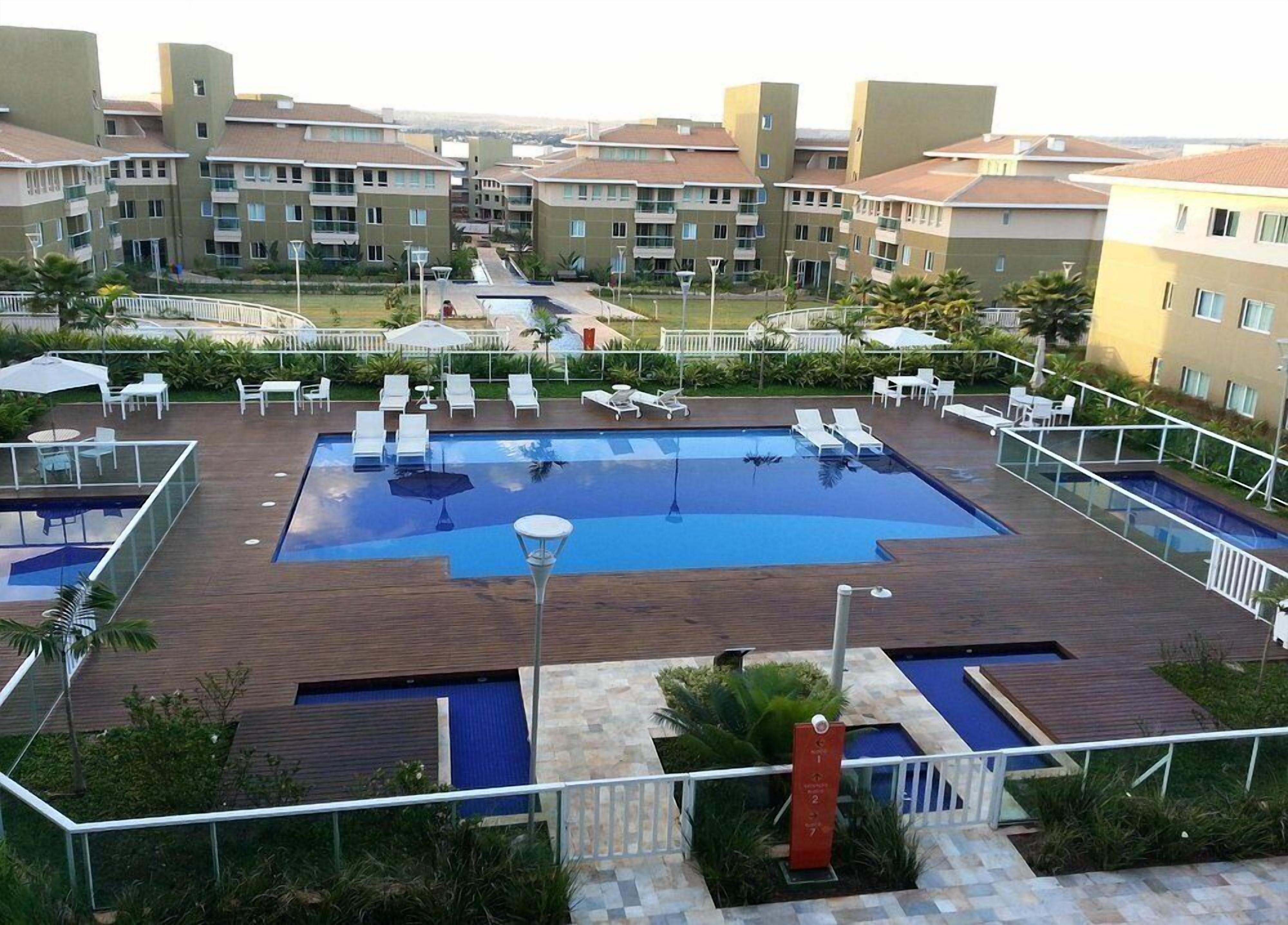 Una piscina en la azotea con varias pistas de natación, rodeada de sillones de descanso y sombrillas, con edificios residenciales como telón de fondo.