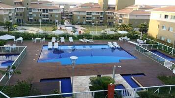 Una piscina en la azotea con varias pistas de natación, rodeada de sillones de descanso y sombrillas, con edificios residenciales como telón de fondo.