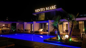 Un hotel moderno con piscina, mobiliario exterior y un llamativo letrero 'VENTO MARE'.
