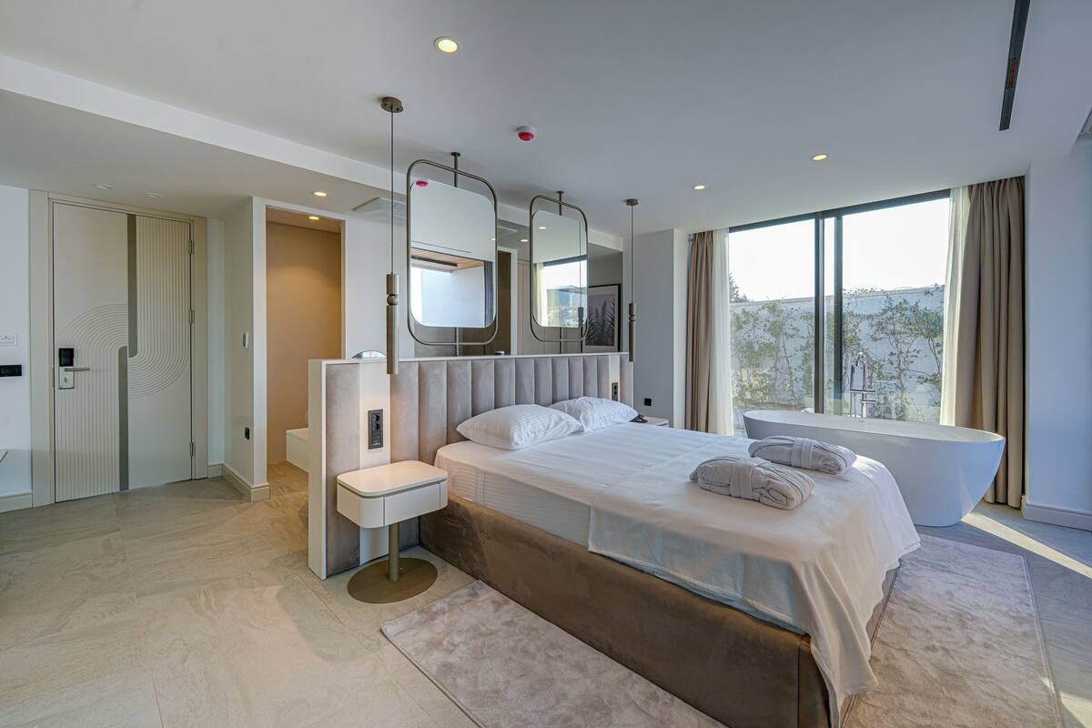 A modern bedroom with a large bed, a built-in bathtub, and a view of the outdoors.
