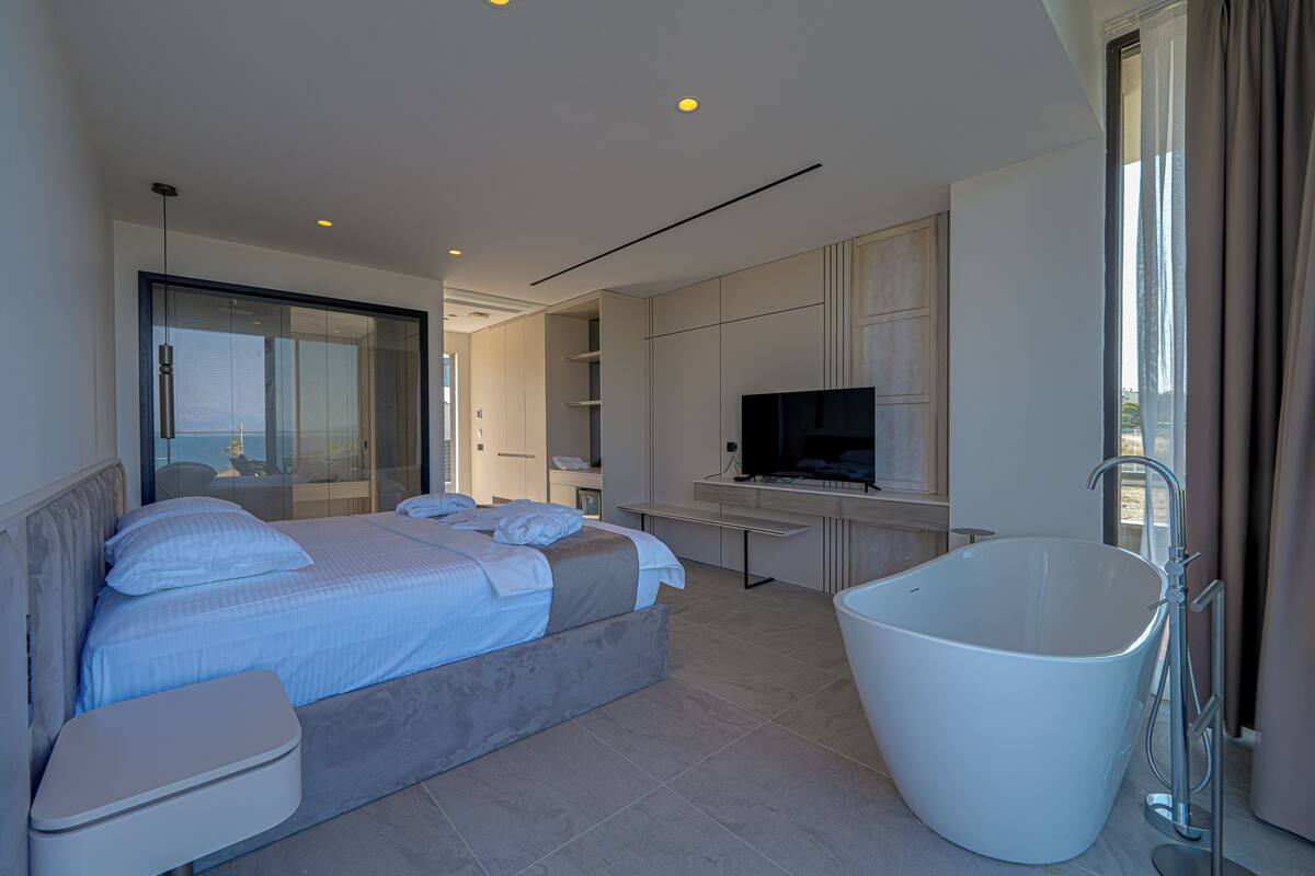 A modern hotel room with a large bed, a separate bathroom with a bathtub, a television, and a large window with curtains.