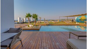 Terraza de madera con piscina, sillas de descanso, palmeras y un mural.