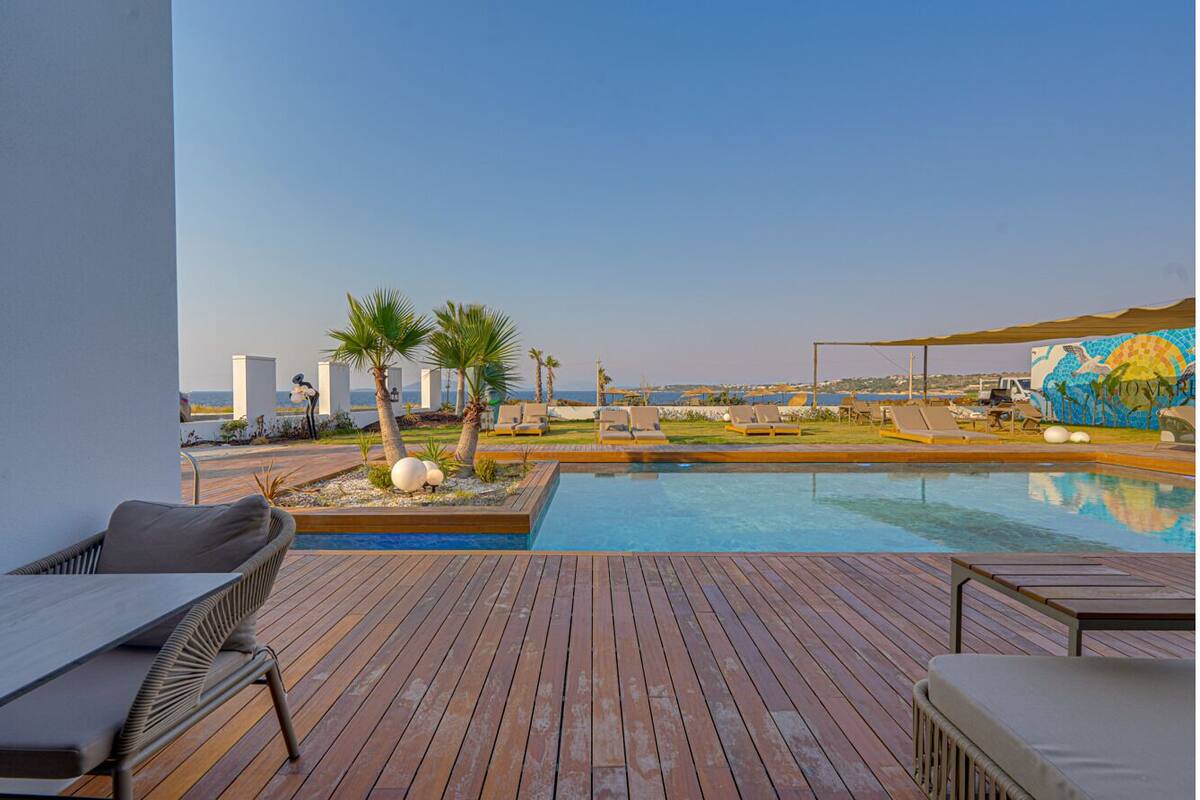 A wooden deck with a pool, lounge chairs, palm trees, and a mural.