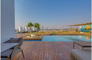 Terraza de madera con piscina, sillas de descanso, palmeras y un mural.