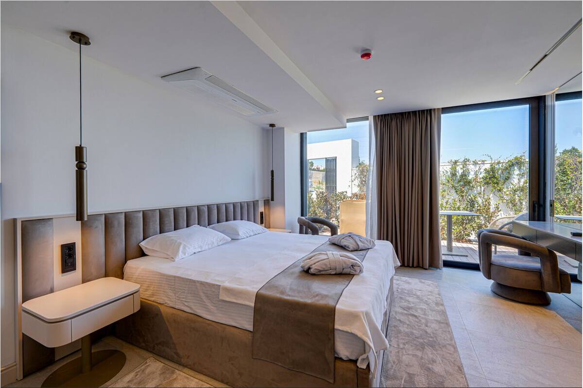 A modern hotel room with a large bed, a desk, and a balcony with a view.