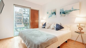 Ein modernes Schlafzimmer mit einem großen Bett, einer Holztür und Blick auf Gebäude durch eine Glastür.