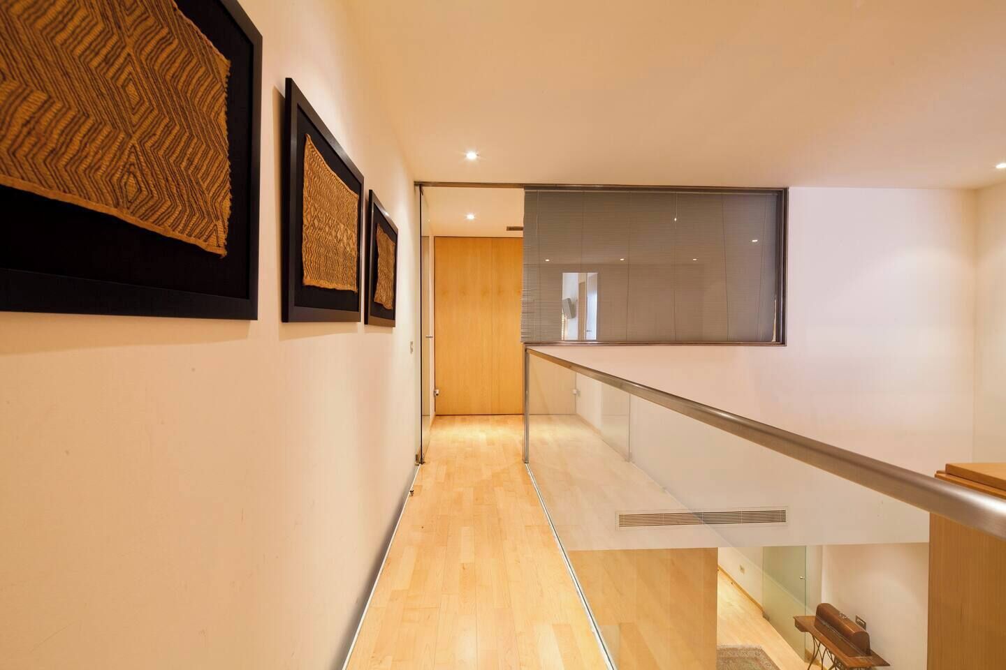 Een moderne hal met houten vloer, kunstwerken in lijsten aan de muren en een glazen balustrade.