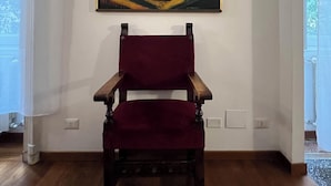 A room with a wooden floor, a red chair, and a painting of a nude figure on the wall.
