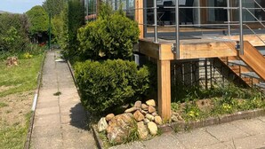 Ein modernes Haus mit Glasfassade, einer Holzterrasse und einem Weg, der dorthin führt.
