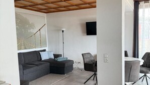 Ein modernes Wohnzimmer mit Holzboden, einem grauen Ecksofa, einem kleinen Tisch und einem an der Wand montierten Fernseher.