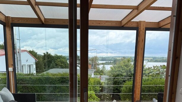 Ein modernes Zimmer mit einer großen Glasdoor, die auf ein Holzdeck mit Blick auf einen See führt.