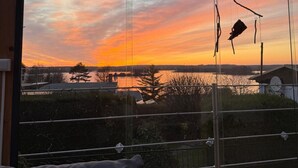 Ein Zimmer mit großem Fenster und Blick auf einen Sonnenuntergang über dem Wasser.