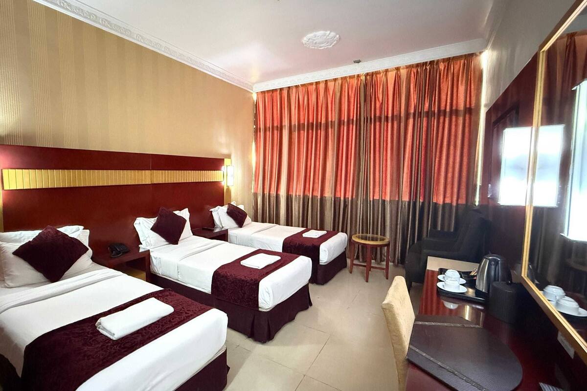 A hotel room with three beds, a marble wall, a large mirror, and a television.