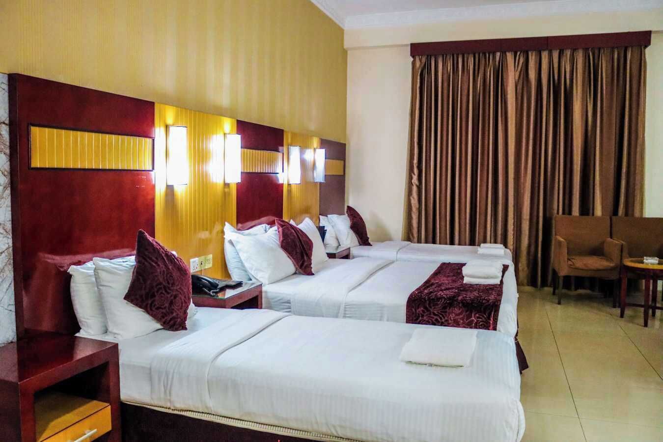 A hotel room with two beds, a desk, a chair, and a large window with curtains.
