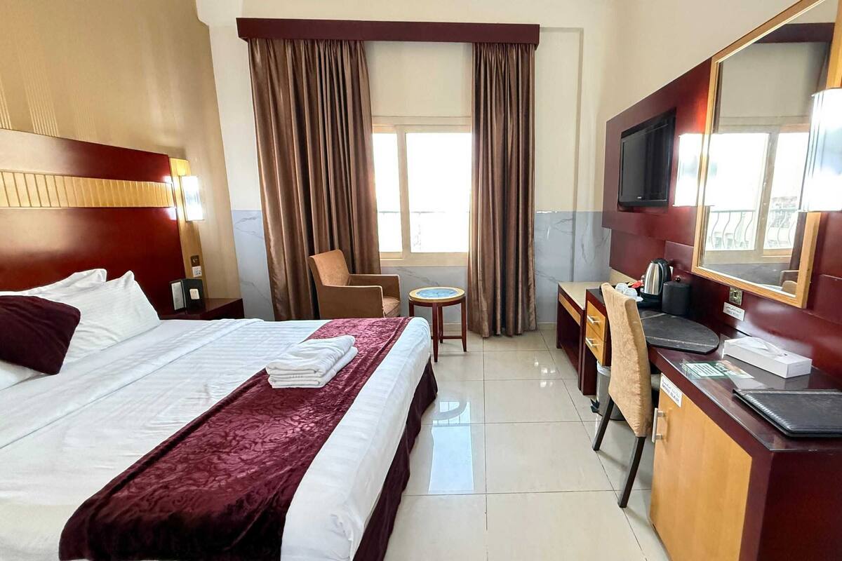 A hotel room with a large bed, a desk, a chair, a TV, and a small table.