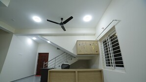 A hotel room with a desk, a chair, a ceiling fan, a staircase, and a window with blinds. - Perambalur Villa  (Perambalūr)